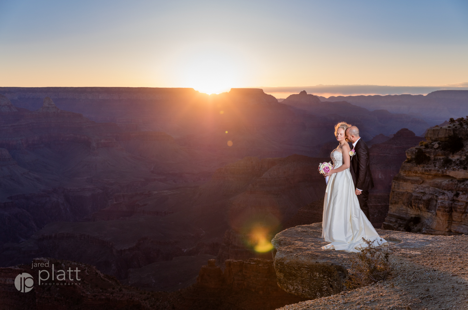 Bride and groom on the edge of the grand canyon at sunrise.